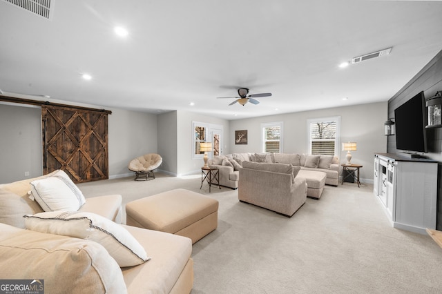 living area with ceiling fan, a barn door, visible vents, and light carpet