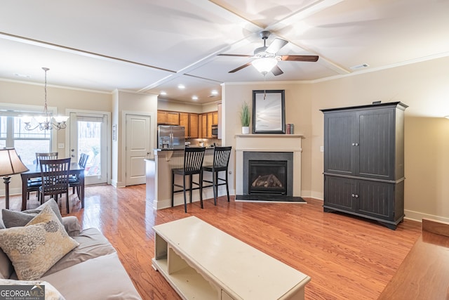 living room featuring ornamental molding, ceiling fan with notable chandelier, and light wood-type flooring