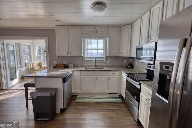 kitchen with light stone countertops, appliances with stainless steel finishes, white cabinetry, sink, and kitchen peninsula