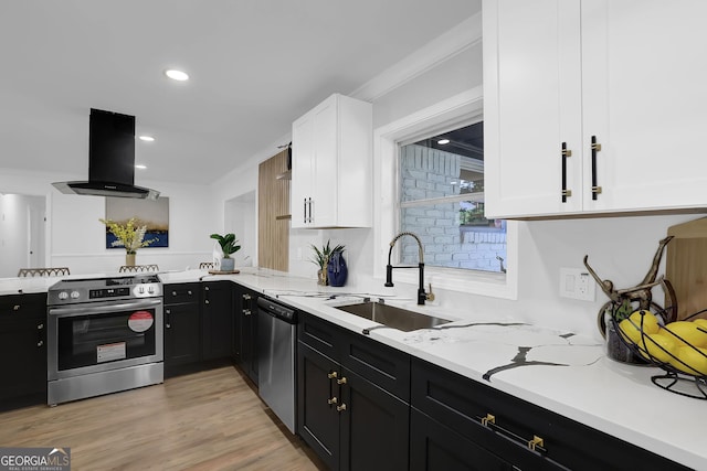 kitchen with white cabinets, appliances with stainless steel finishes, island exhaust hood, sink, and light hardwood / wood-style flooring