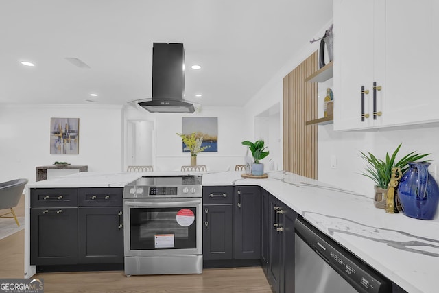 kitchen with island exhaust hood, appliances with stainless steel finishes, white cabinets, light stone countertops, and light hardwood / wood-style flooring