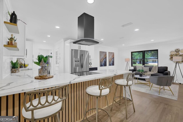 kitchen with light stone countertops, kitchen peninsula, stainless steel fridge, and island range hood