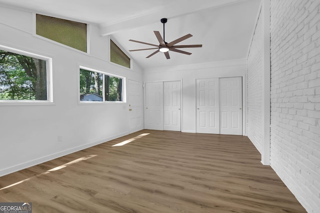 unfurnished bedroom with brick wall, dark wood-type flooring, two closets, lofted ceiling with beams, and ceiling fan