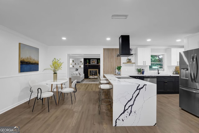 kitchen with white cabinetry, island exhaust hood, a brick fireplace, appliances with stainless steel finishes, and built in features