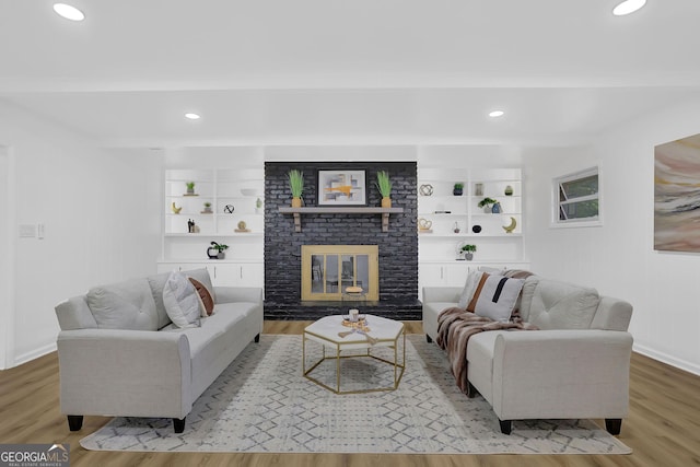 living room featuring a brick fireplace, built in shelves, and light hardwood / wood-style flooring