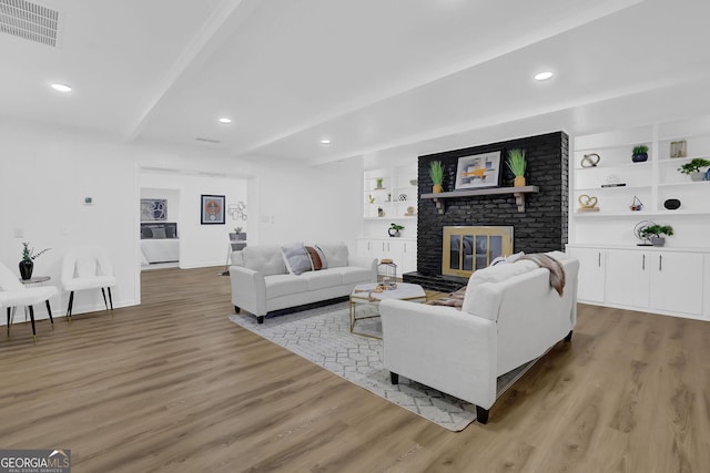 living room with built in shelves, a fireplace, beamed ceiling, and light hardwood / wood-style flooring