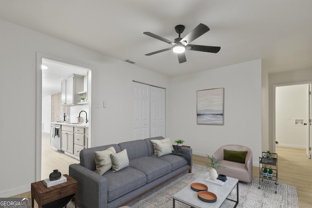 living room with light wood-type flooring, ceiling fan, and sink