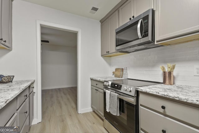 kitchen with light wood-type flooring, appliances with stainless steel finishes, gray cabinetry, and light stone countertops