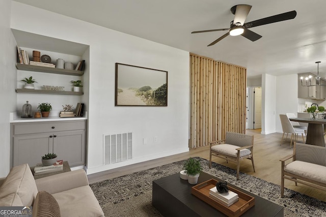 living room featuring visible vents, ceiling fan with notable chandelier, light wood-type flooring, and baseboards