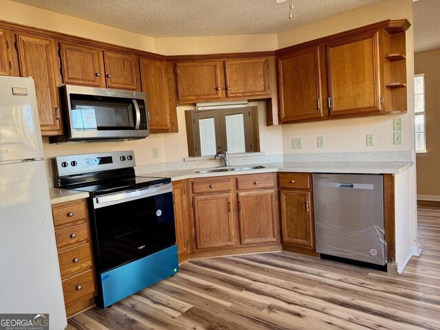 kitchen featuring light wood-type flooring, sink, stainless steel appliances, and a textured ceiling