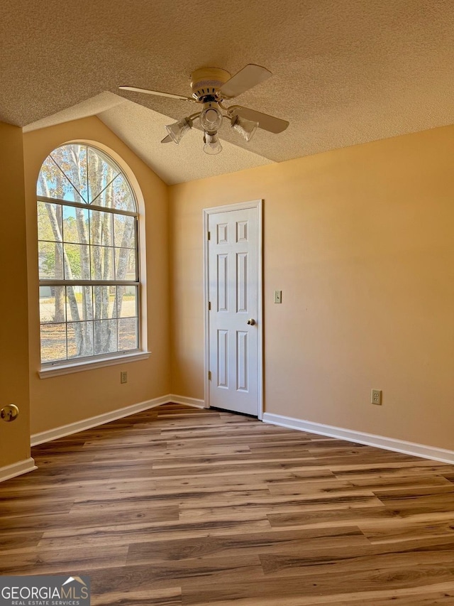 empty room featuring ceiling fan, hardwood / wood-style flooring, vaulted ceiling, and a textured ceiling