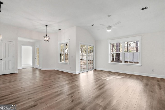 unfurnished living room featuring ceiling fan with notable chandelier, plenty of natural light, vaulted ceiling, and dark wood-type flooring