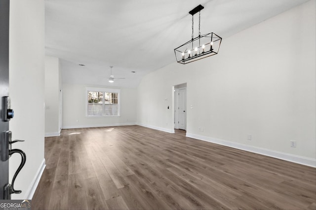 unfurnished living room with ceiling fan with notable chandelier, dark hardwood / wood-style floors, and vaulted ceiling