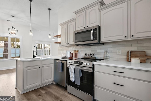 kitchen featuring appliances with stainless steel finishes, decorative light fixtures, decorative backsplash, sink, and kitchen peninsula