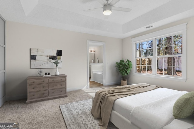 carpeted bedroom featuring ceiling fan, a tray ceiling, and ensuite bath