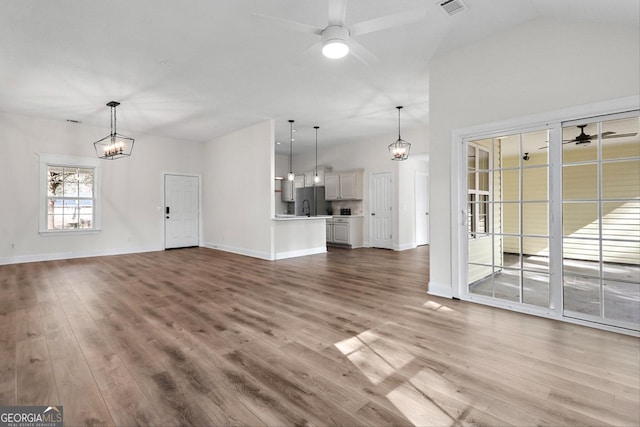 unfurnished living room featuring vaulted ceiling, sink, ceiling fan with notable chandelier, and hardwood / wood-style floors