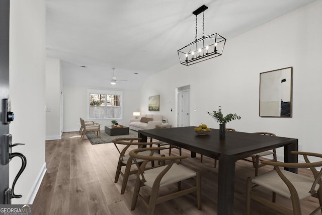 dining area with ceiling fan with notable chandelier, hardwood / wood-style floors, and lofted ceiling