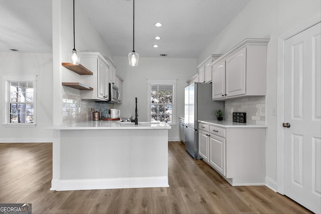 kitchen with pendant lighting, kitchen peninsula, decorative backsplash, stainless steel appliances, and white cabinets