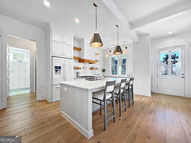 kitchen featuring white cabinetry, hanging light fixtures, light wood-type flooring, a breakfast bar area, and white fridge with ice dispenser