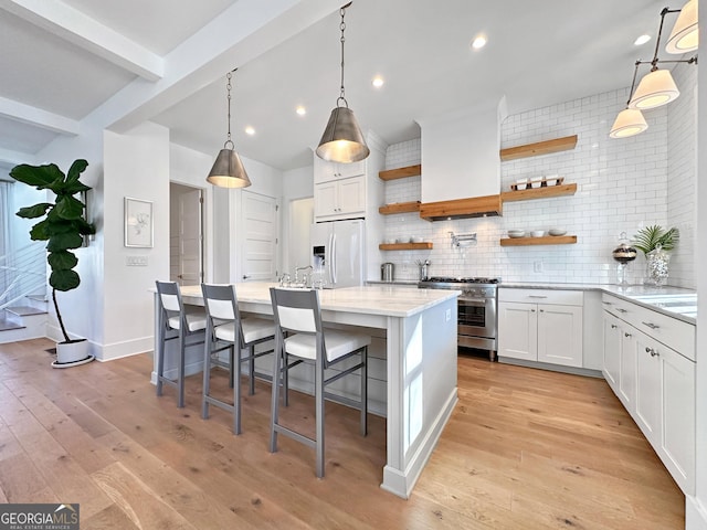 kitchen featuring a center island, decorative backsplash, stainless steel range, white cabinets, and white fridge with ice dispenser