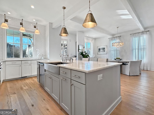 kitchen featuring decorative light fixtures, sink, a kitchen island with sink, and beamed ceiling