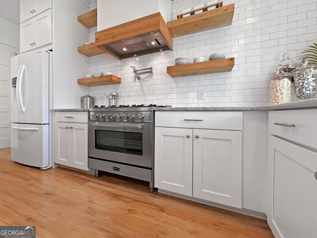 kitchen with backsplash, premium range hood, high end range, white refrigerator with ice dispenser, and white cabinets