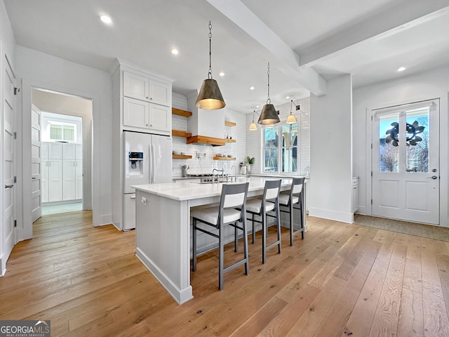 kitchen featuring decorative light fixtures, a breakfast bar, white cabinetry, a healthy amount of sunlight, and white refrigerator with ice dispenser