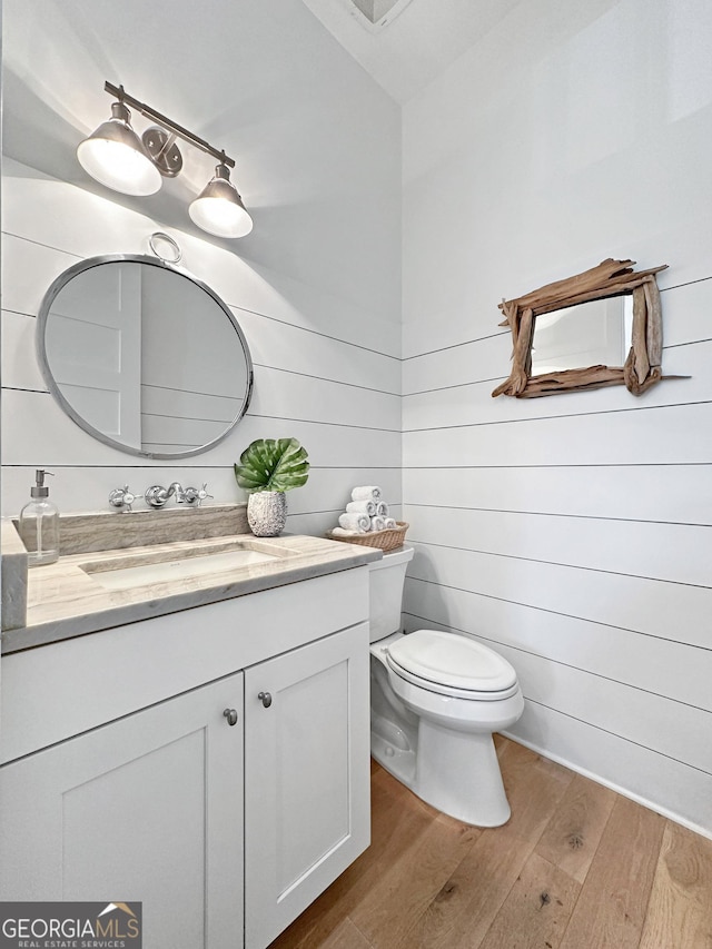 bathroom featuring toilet, wooden walls, hardwood / wood-style flooring, and vanity