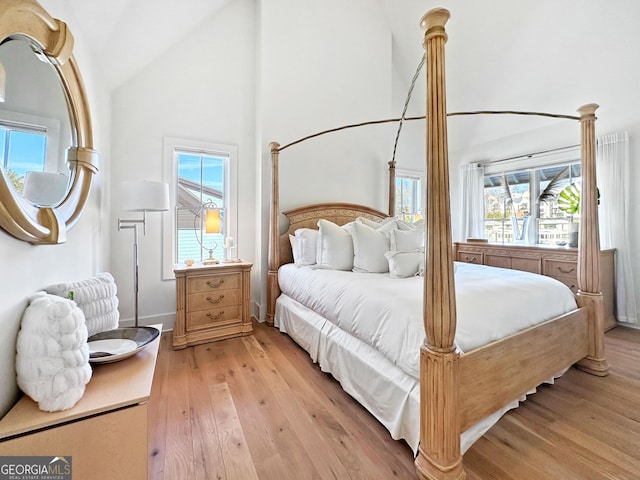 bedroom with high vaulted ceiling, multiple windows, and light hardwood / wood-style floors