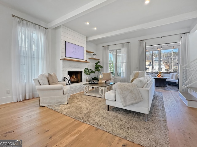 living room with a brick fireplace, beam ceiling, and light hardwood / wood-style flooring