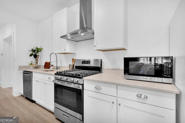 kitchen with stainless steel appliances, sink, white cabinetry, and wall chimney range hood