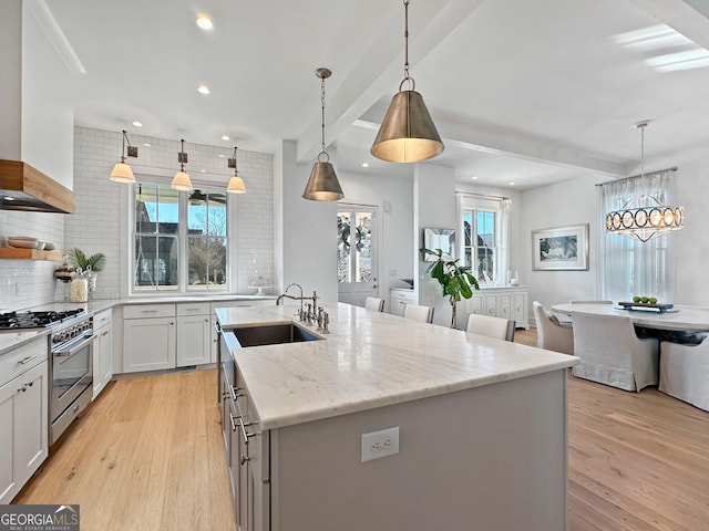 kitchen featuring pendant lighting, custom exhaust hood, stainless steel range, an island with sink, and sink