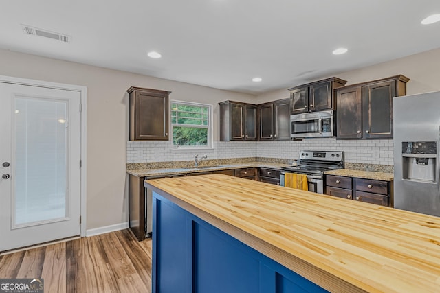 kitchen featuring light wood-type flooring, wooden counters, stainless steel appliances, and dark brown cabinets