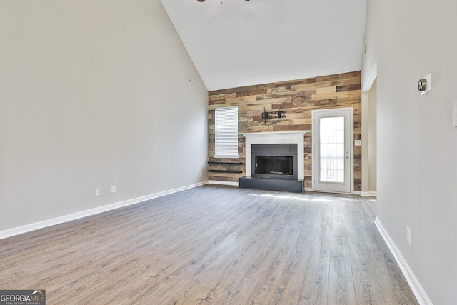 unfurnished living room with ceiling fan, a fireplace, wooden walls, light hardwood / wood-style flooring, and high vaulted ceiling