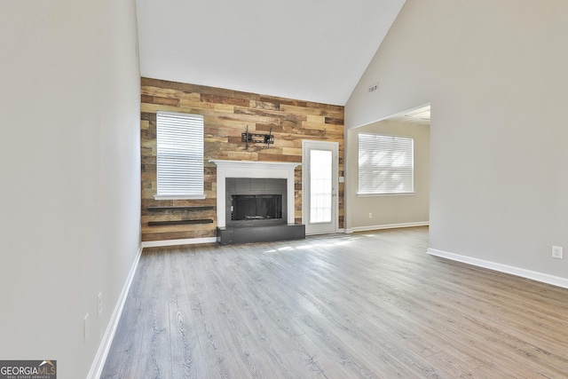 unfurnished living room with wood-type flooring, a fireplace, wood walls, and high vaulted ceiling