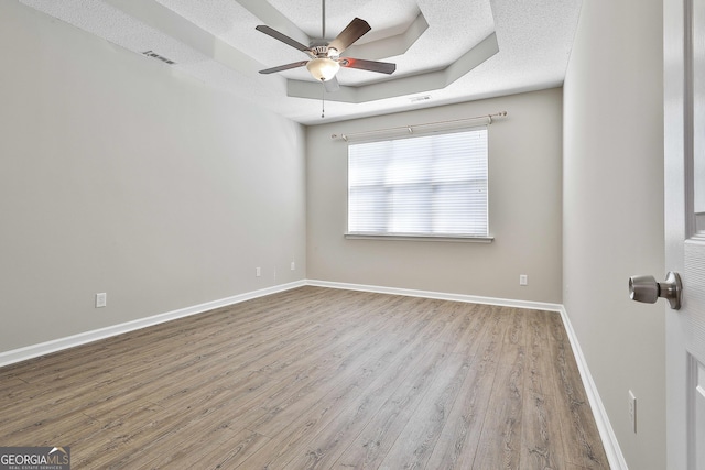 unfurnished room with a textured ceiling, ceiling fan, a raised ceiling, and light wood-type flooring