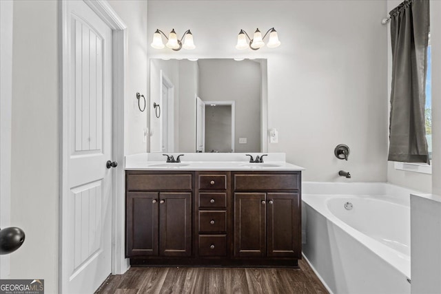 full bath featuring double vanity, a garden tub, a sink, and wood finished floors