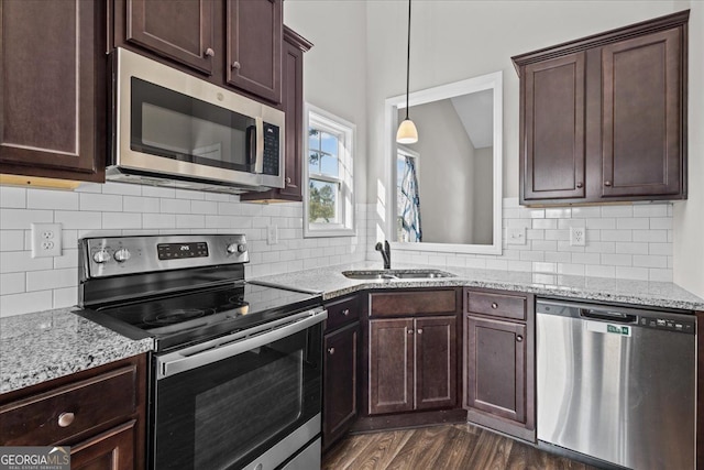 kitchen featuring light stone counters, pendant lighting, dark wood finished floors, stainless steel appliances, and a sink