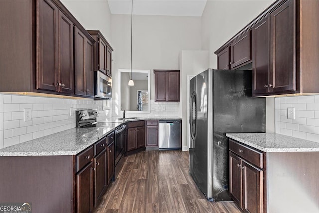 kitchen with light stone counters, dark wood-style floors, pendant lighting, appliances with stainless steel finishes, and a sink