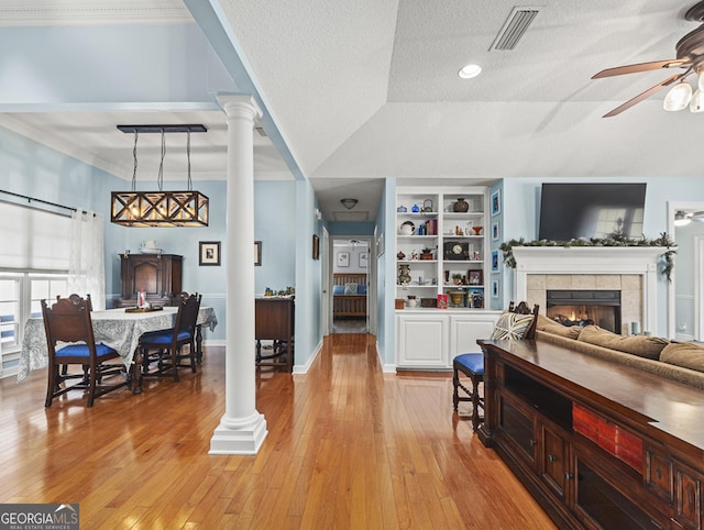 living room featuring ceiling fan, a tile fireplace, built in features, and light wood-type flooring