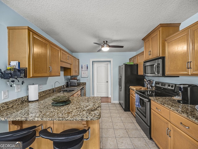 kitchen featuring light tile patterned floors, a kitchen bar, ceiling fan, stainless steel appliances, and dark stone countertops