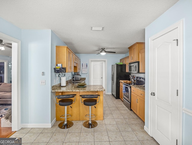 kitchen featuring a textured ceiling, stone counters, stainless steel appliances, and a breakfast bar area