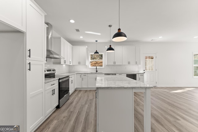 kitchen featuring electric stove, a center island, white cabinetry, light wood-style floors, and wall chimney range hood