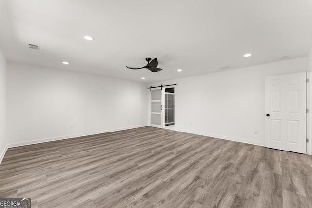 empty room featuring recessed lighting, a barn door, visible vents, and wood finished floors