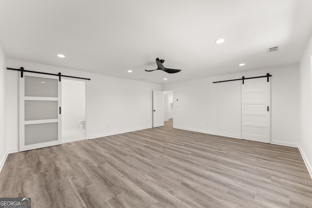 unfurnished bedroom with baseboards, visible vents, light wood-style flooring, recessed lighting, and a barn door