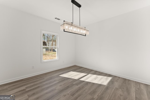 unfurnished dining area with an inviting chandelier, wood finished floors, visible vents, and baseboards