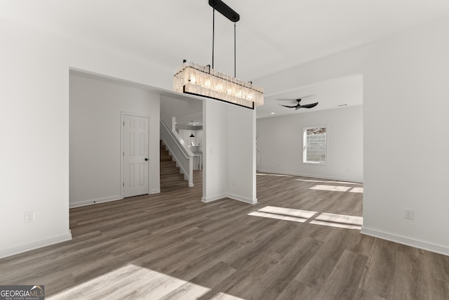 unfurnished dining area featuring stairway, a ceiling fan, baseboards, and wood finished floors