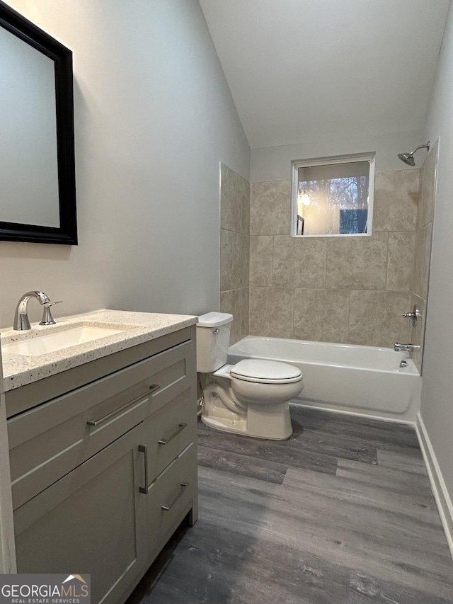 full bathroom with tiled shower / bath, vanity, toilet, vaulted ceiling, and hardwood / wood-style flooring