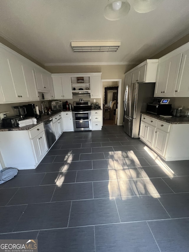 kitchen with white cabinets, appliances with stainless steel finishes, crown molding, and dark tile patterned floors