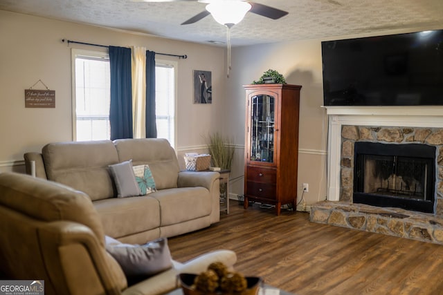 living room featuring ceiling fan, wood-type flooring, a fireplace, and a textured ceiling